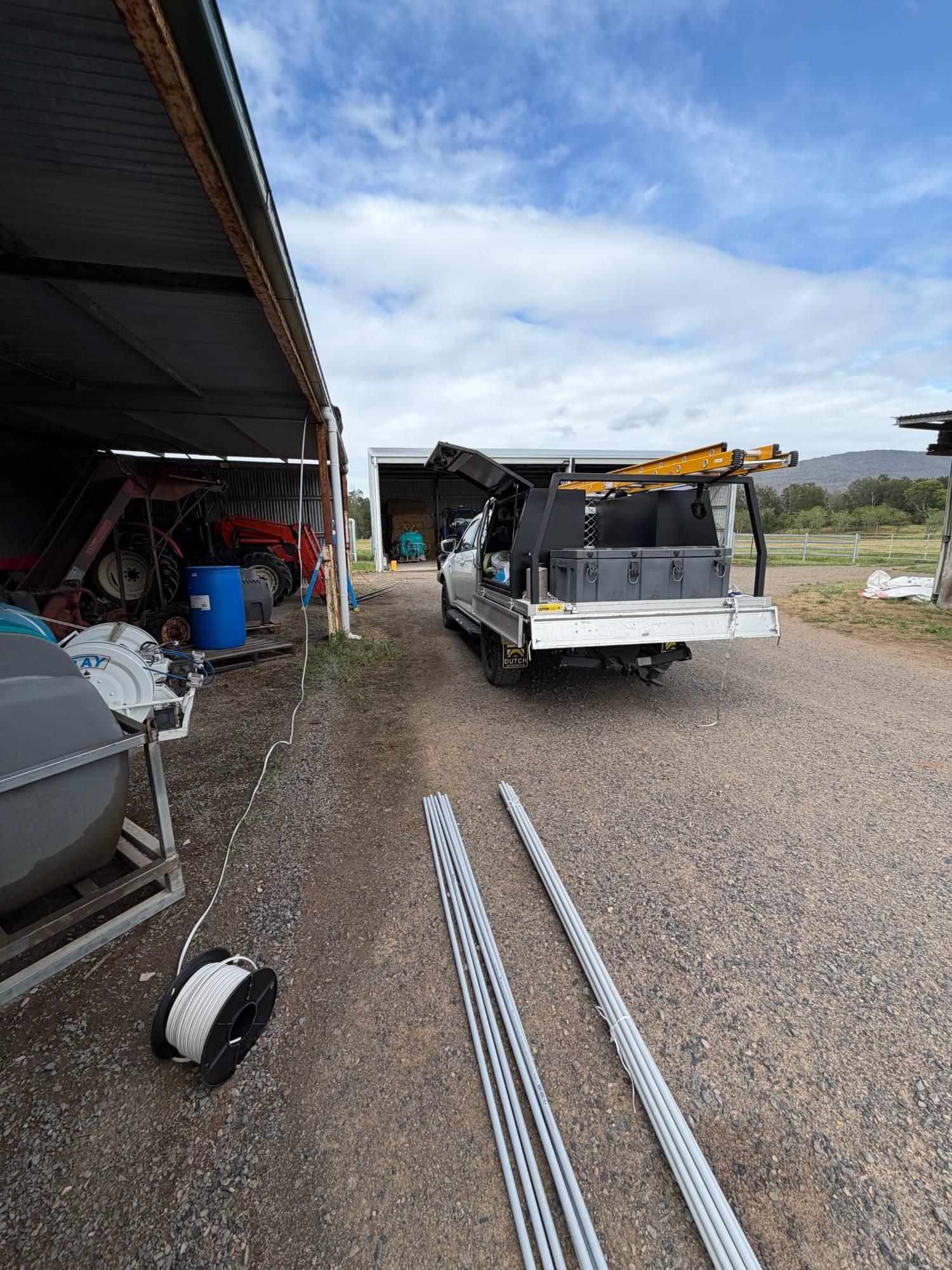 Lengths of grey conduit and a reel of cable laid out beside the ute at a farm shed