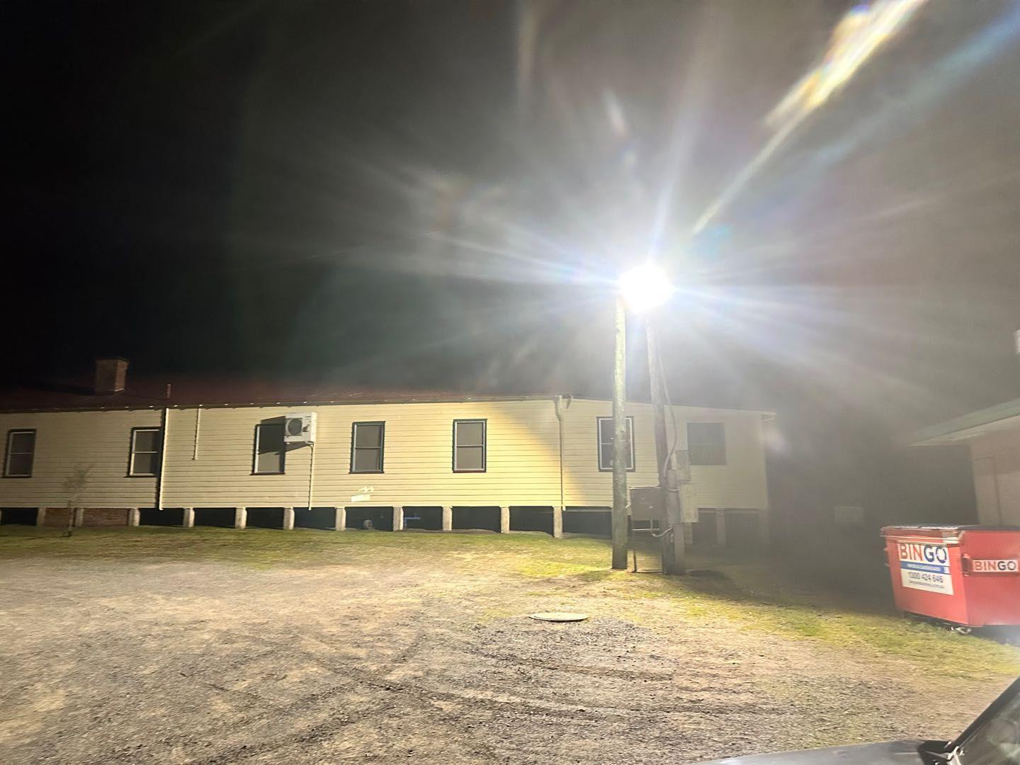 LED floodlight on a pole lighting a gravel yard and building at night