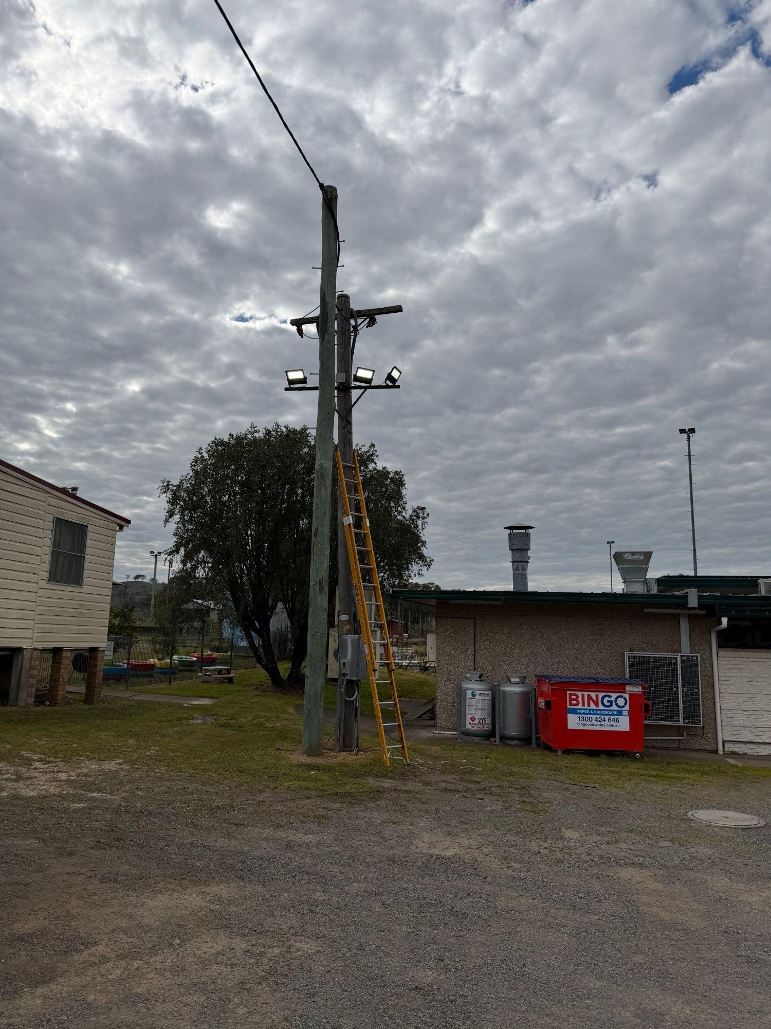 Three LED floodlights on a crossarm on a timber pole, with a ladder against the pole