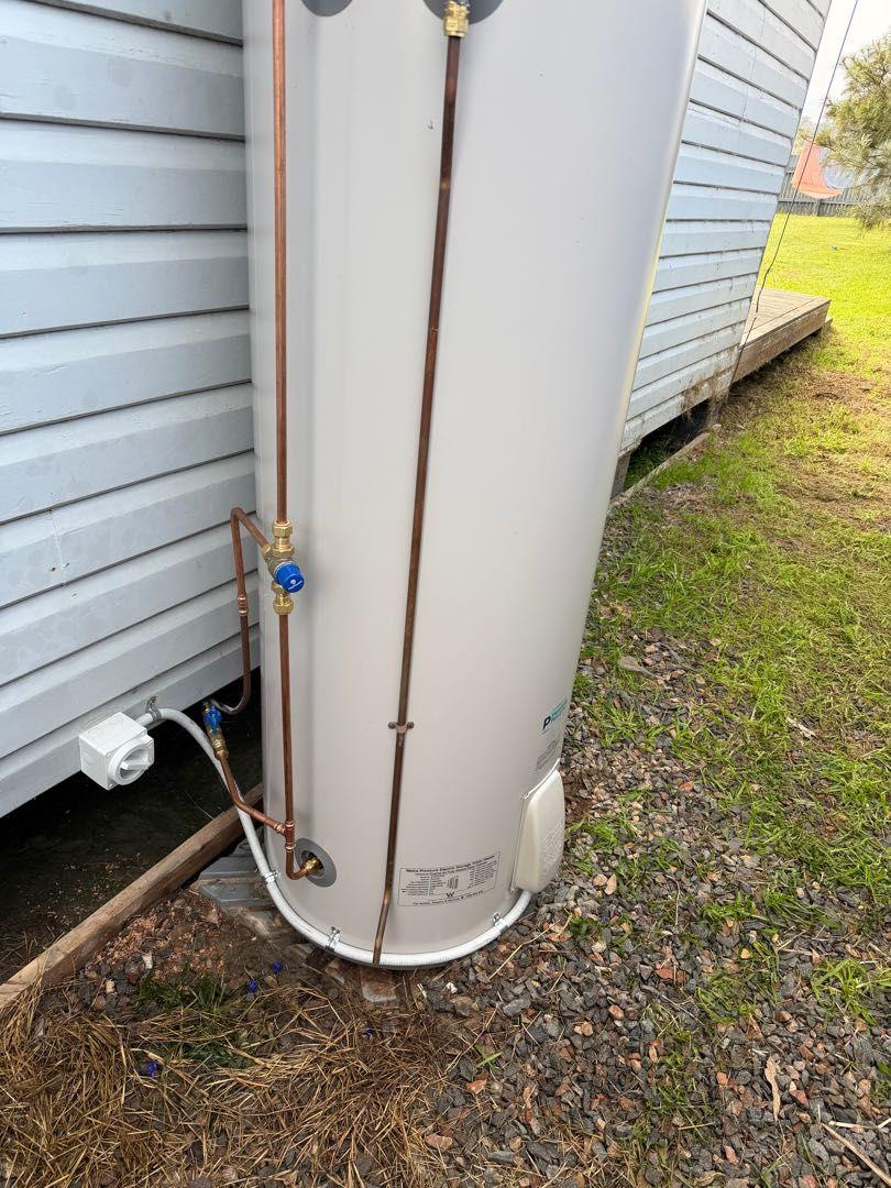 Electric hot water system installed outside a weatherboard building
