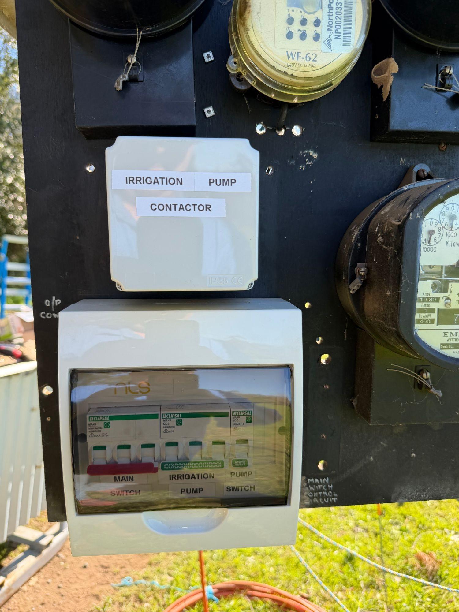 Labelled irrigation pump contactor above a small switchboard with main switch, irrigation pump and pump switch breakers, beside the meters on a farm meter panel