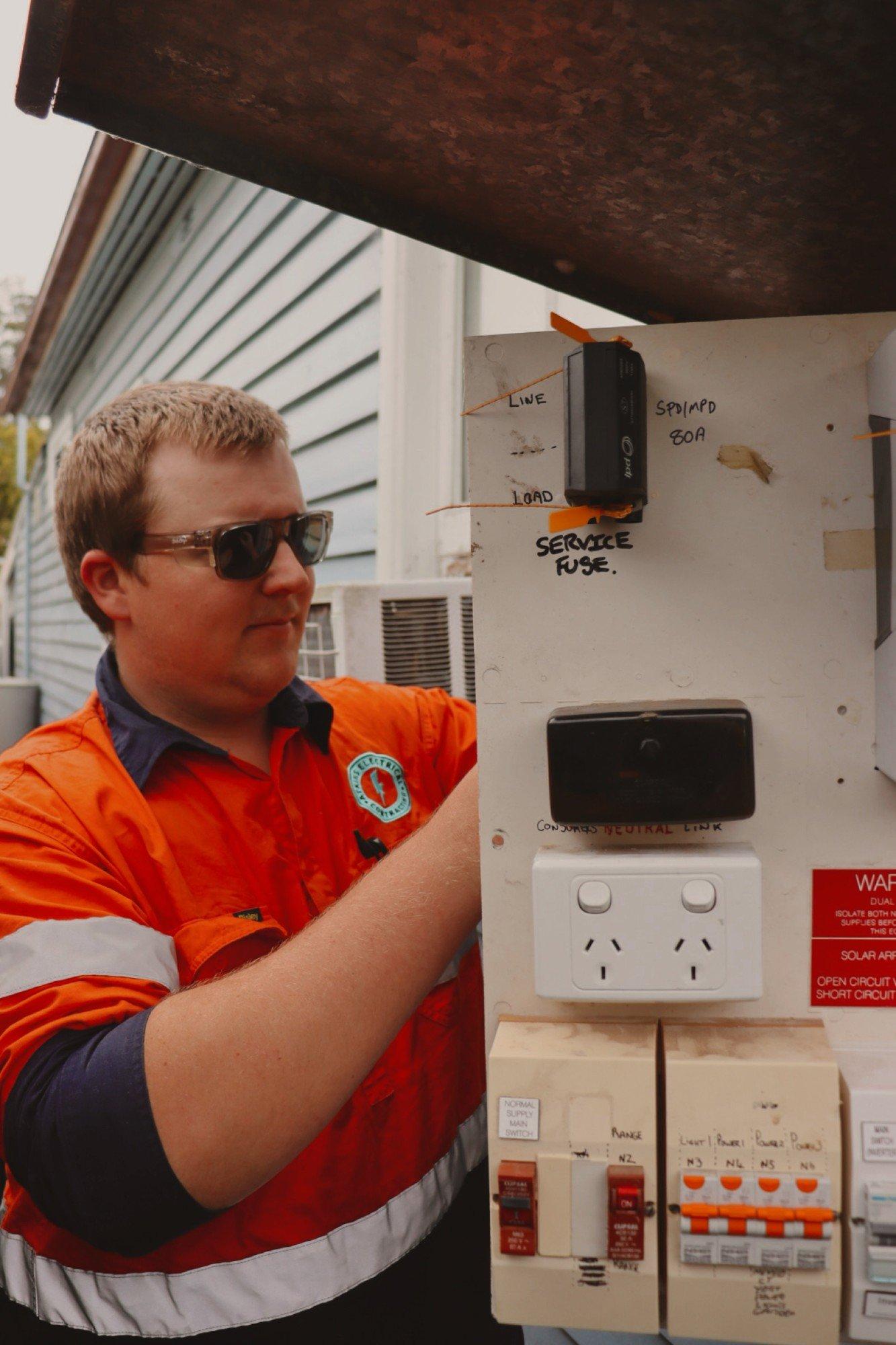Kayden Atkins in hi-vis working on a switchboard outside a weatherboard house