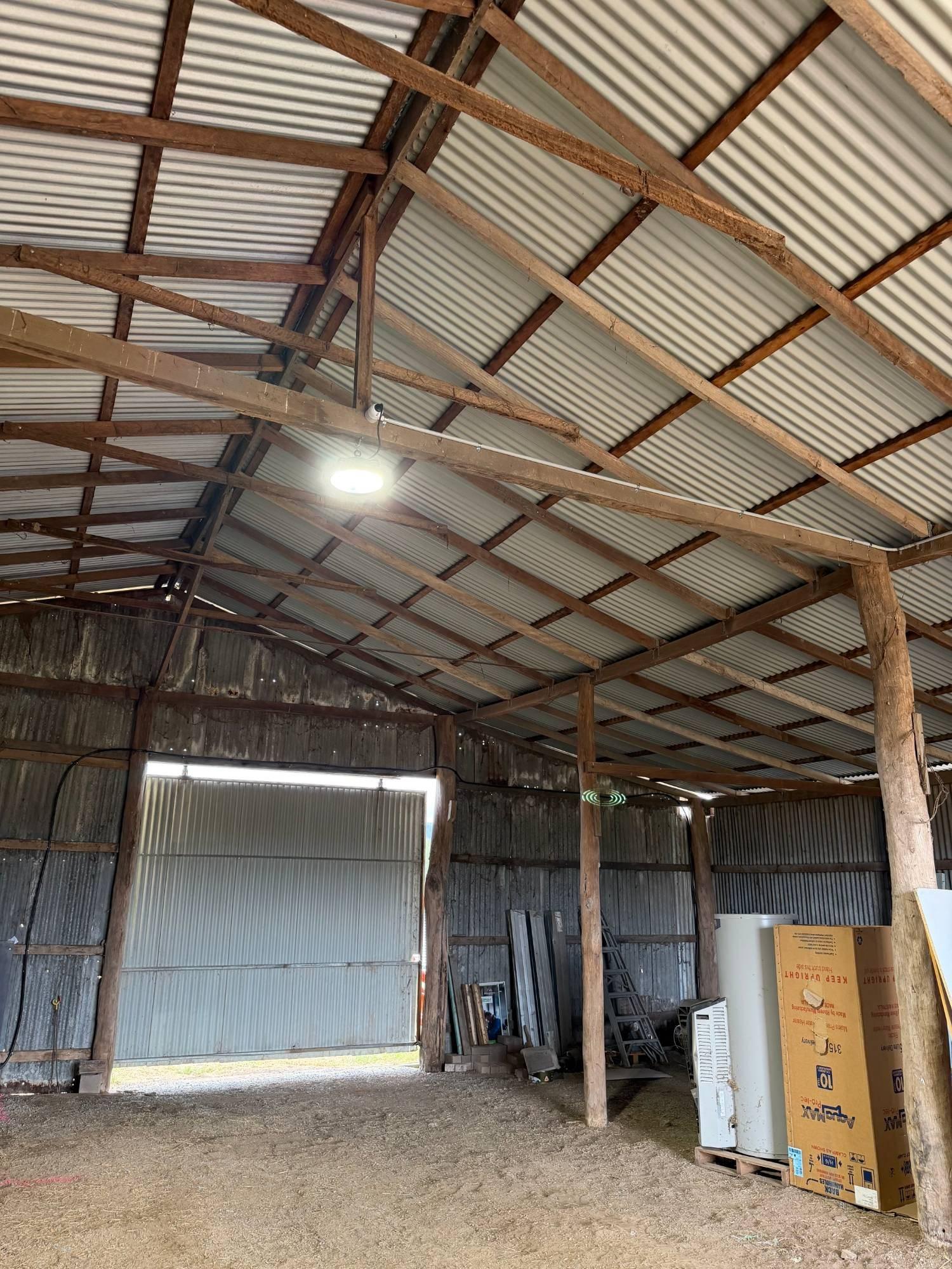 LED high-bay light fitted to a timber beam in a machinery shed, with conduit run along the beam